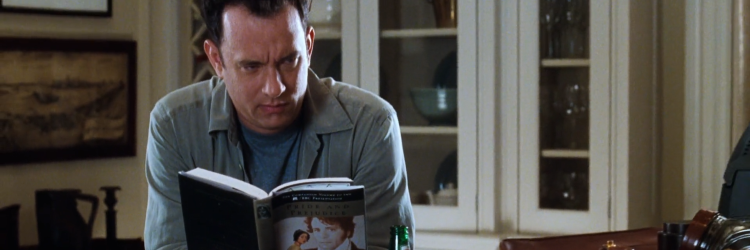 Fotograma de la película Tienes un e-mail. Vemos al personaje de Joe Fox, interpretado por Tom Hanks, sentado en una mesa en su casa mientras lee Orgullo y prejuicio y pone cara de desagrado.